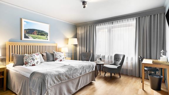 Hotellrum med dubbelsäng, ett skrivbord och två fåtöljer.