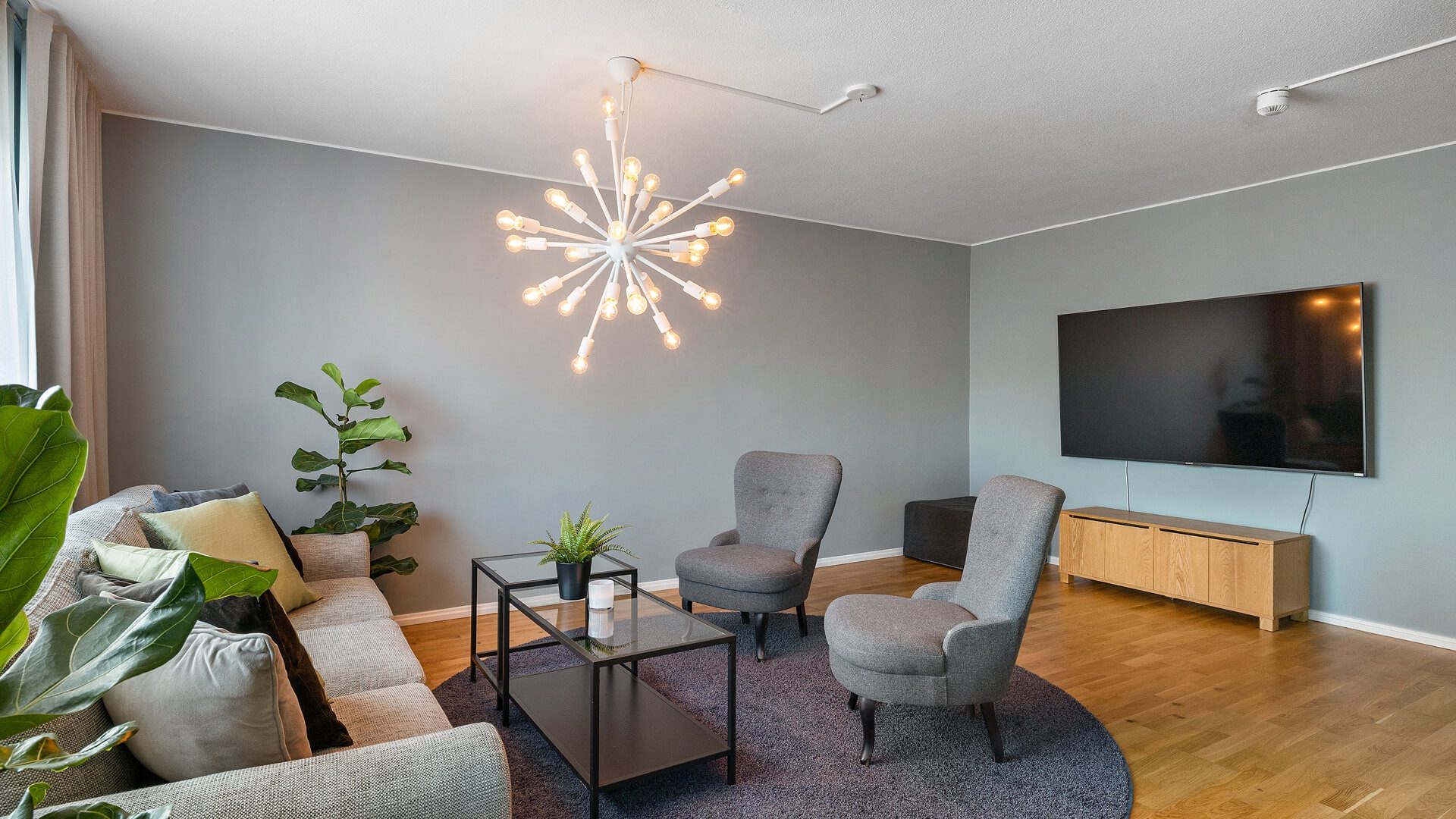 Ett vardagsrum i ett hotellrum. Soffa, soffbord, två fåtöljer och en tv på väggen.