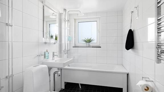 Ett badrum i ett hotellrum. Toalett, handfat, badkar. Helkaklat i vitt.