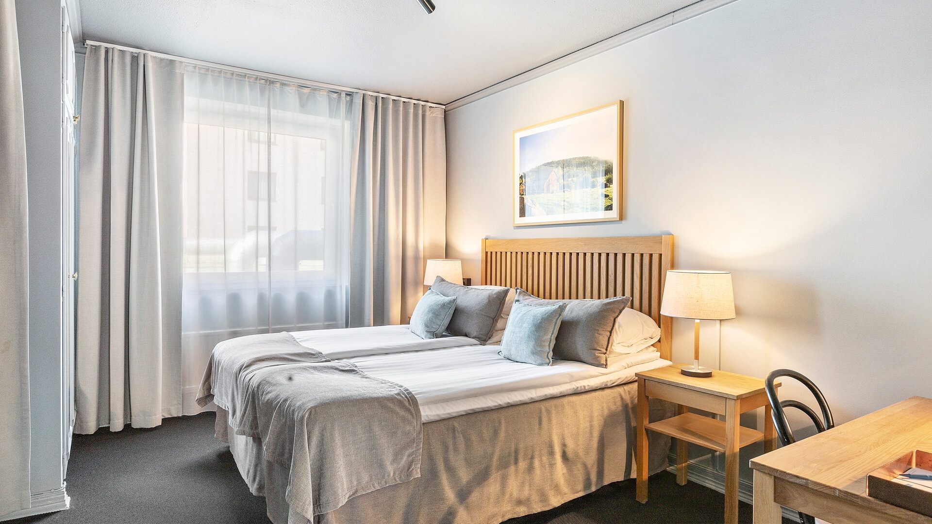 En dubbelsäng i ett hotellrum. Ett nattduksbord med en lampa står bredvid sängen.