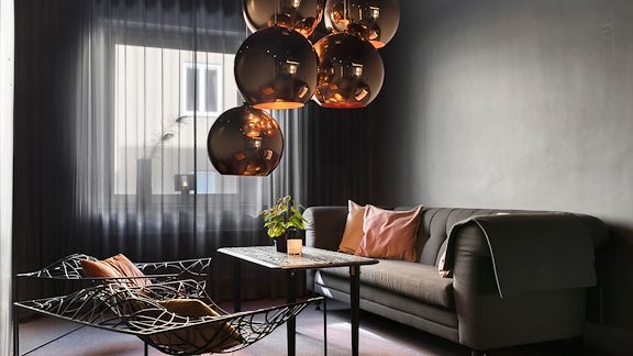 En soffa, ett bord och två designerstolar. Från taket hänger en guldig lampa.